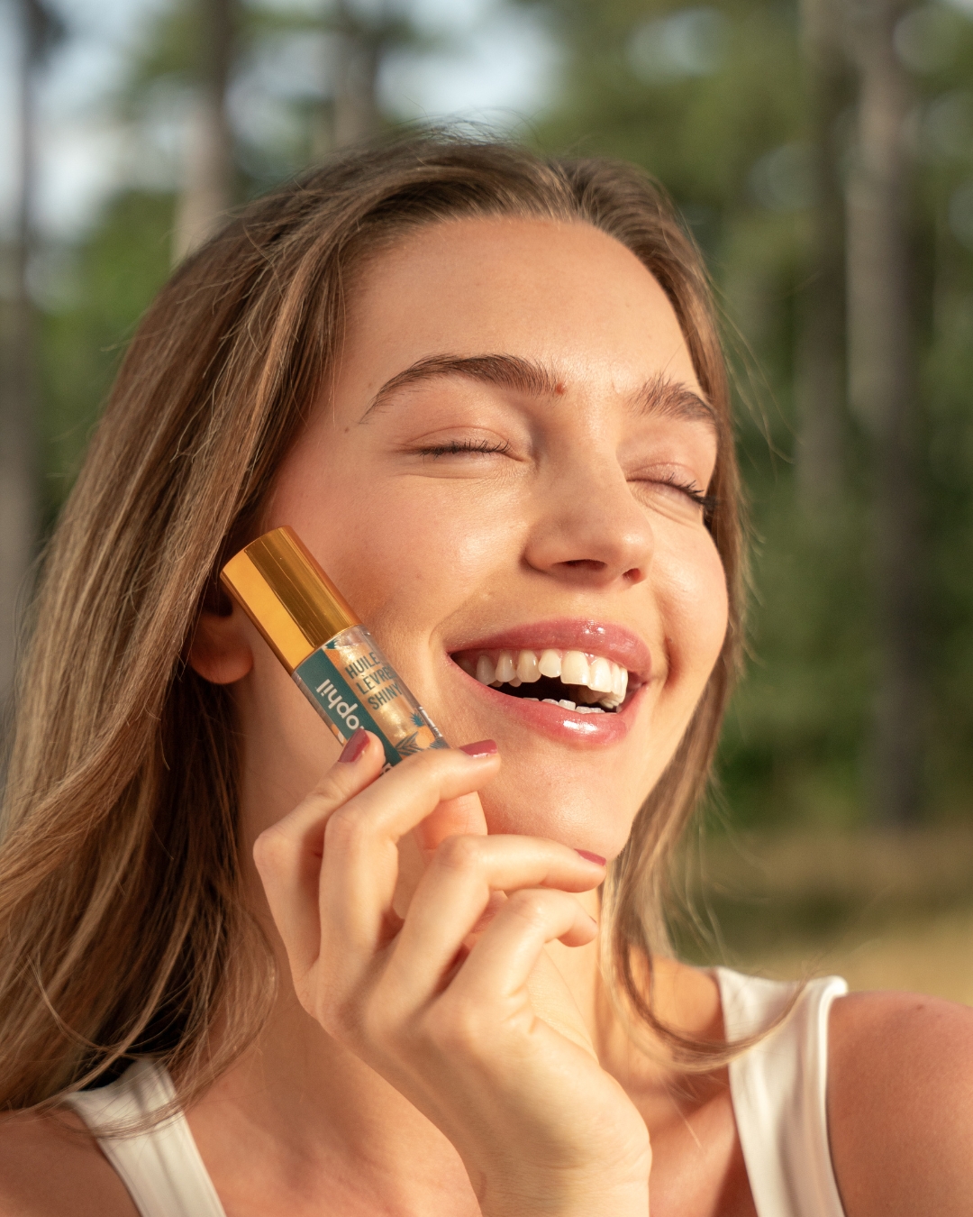 Smiling young woman holding Dermophil Shiny lip oil in her hand